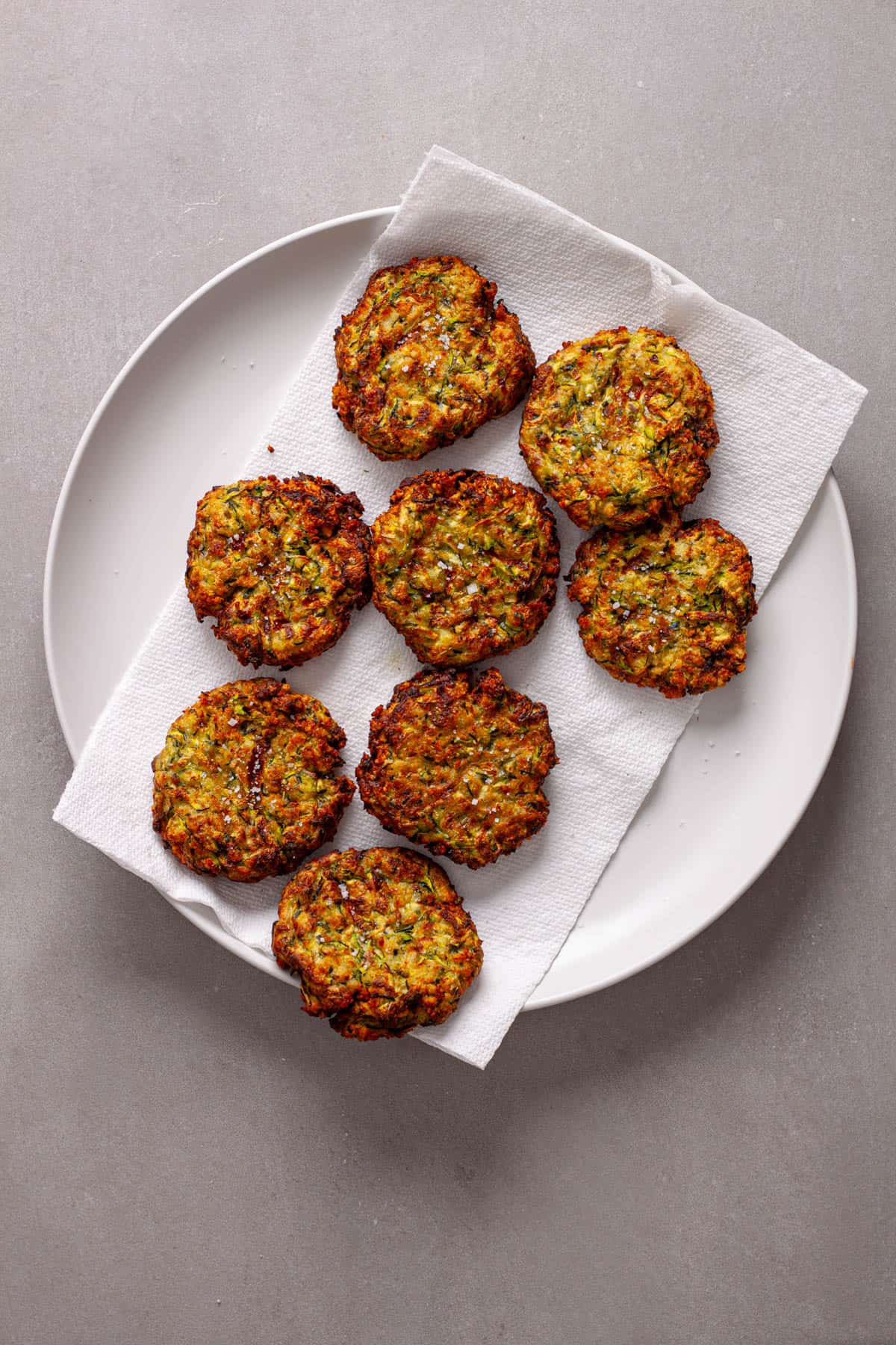Air fryer zucchini fritters drying on a paper towel lined plate.