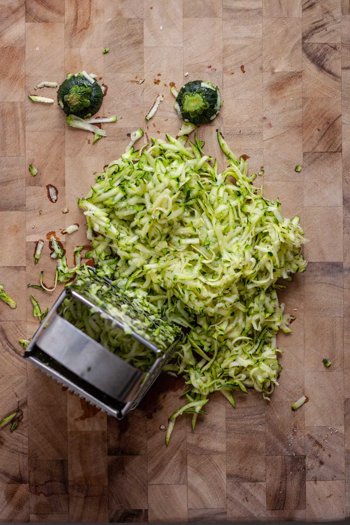 A couple zucchinis grated on a wooden cutting board.