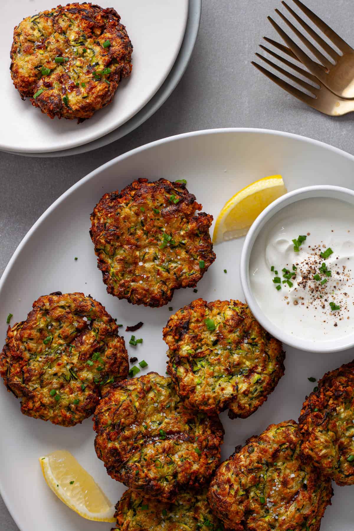 Air-fryer zucchini fritters on a white plate with sour cream topped with chives to the side.