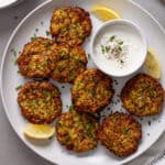 A platter of air fryer zucchini fritters with sour cream and chive dip to the side and lemon wedges as garnish.