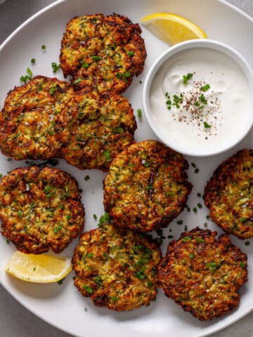 A platter of air fryer zucchini fritters with sour cream and chive dip to the side and lemon wedges as garnish.