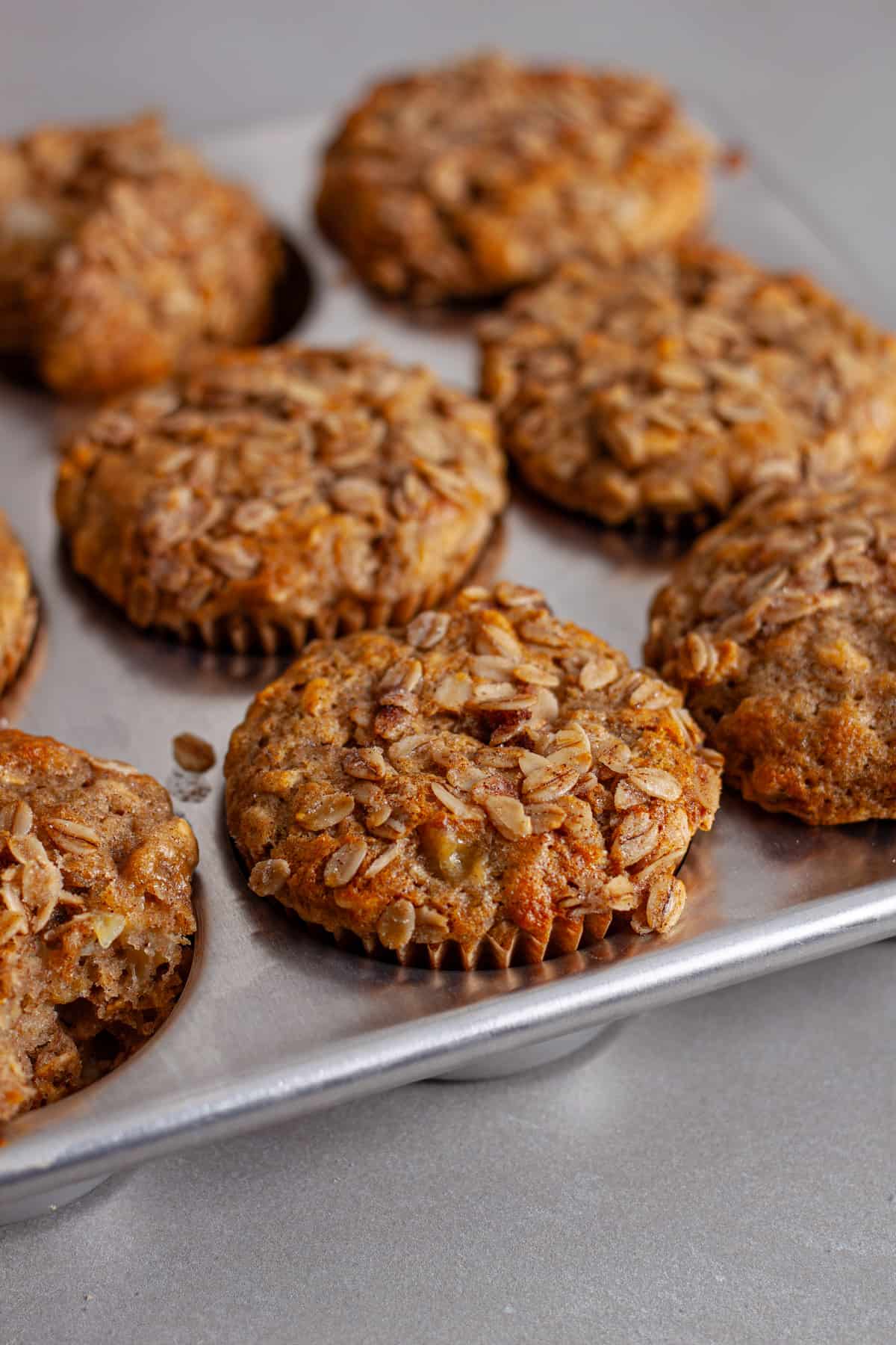 A muffin tin with banana oatmeal muffins inside topped with crunchy oats.