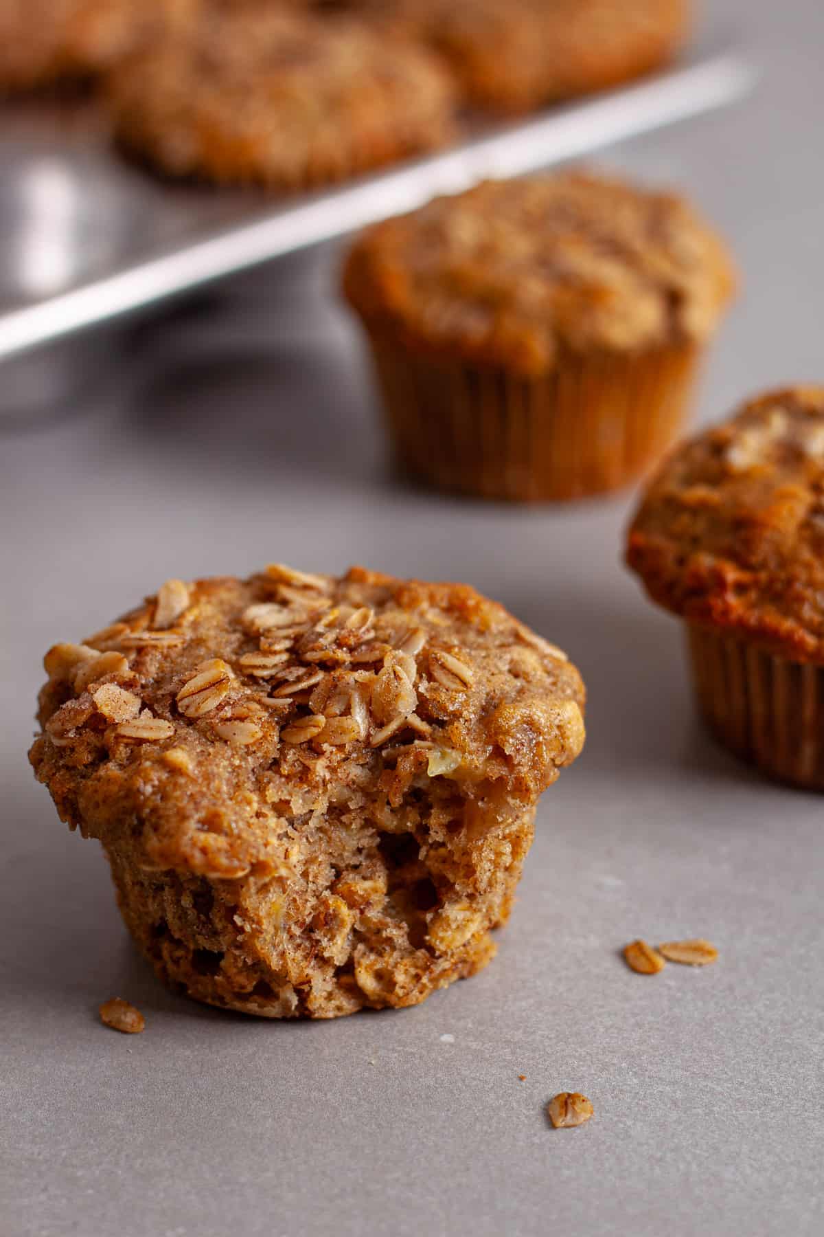 A bite taken out of a banana oatmeal muffin on a gray table with more muffins in the background.