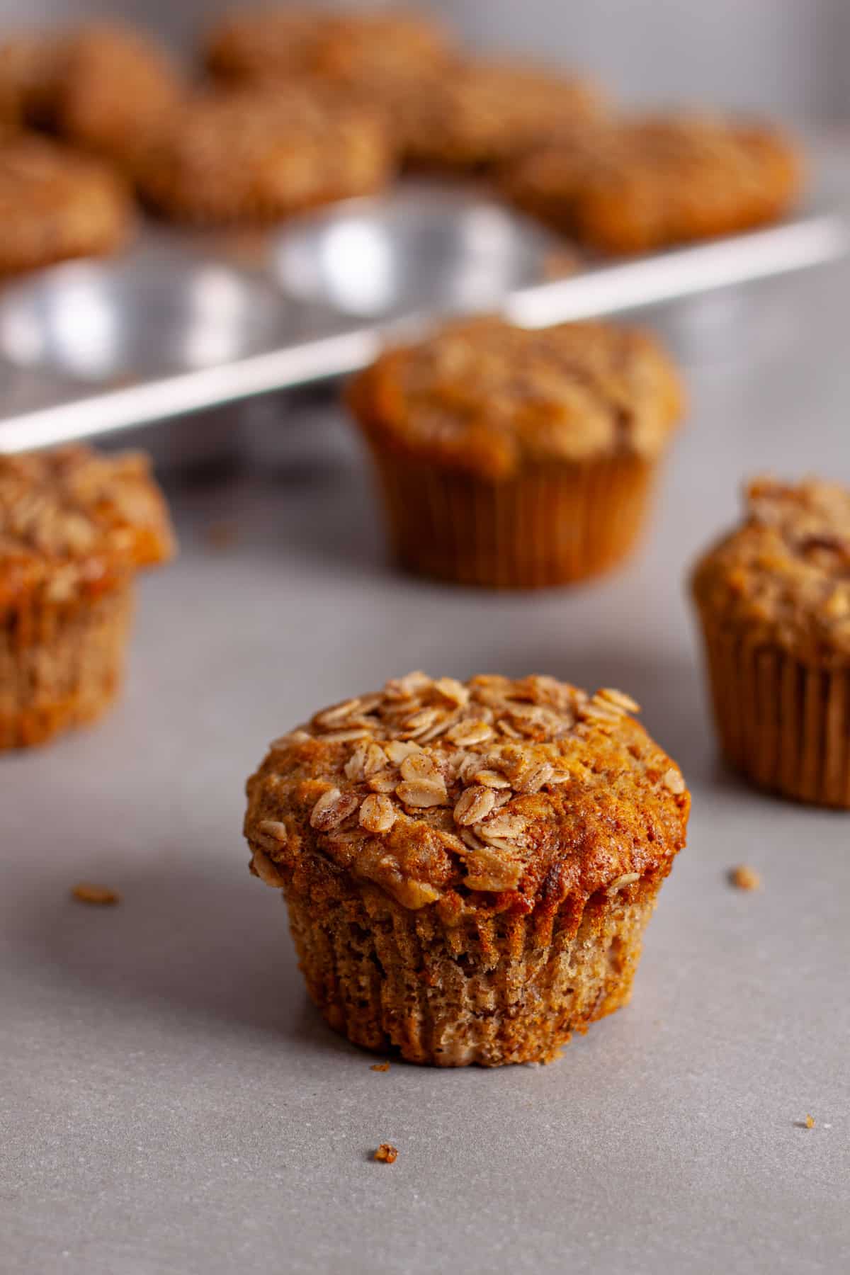 Banana oat muffins on a gray table with a muffin tin of more muffins in the background.