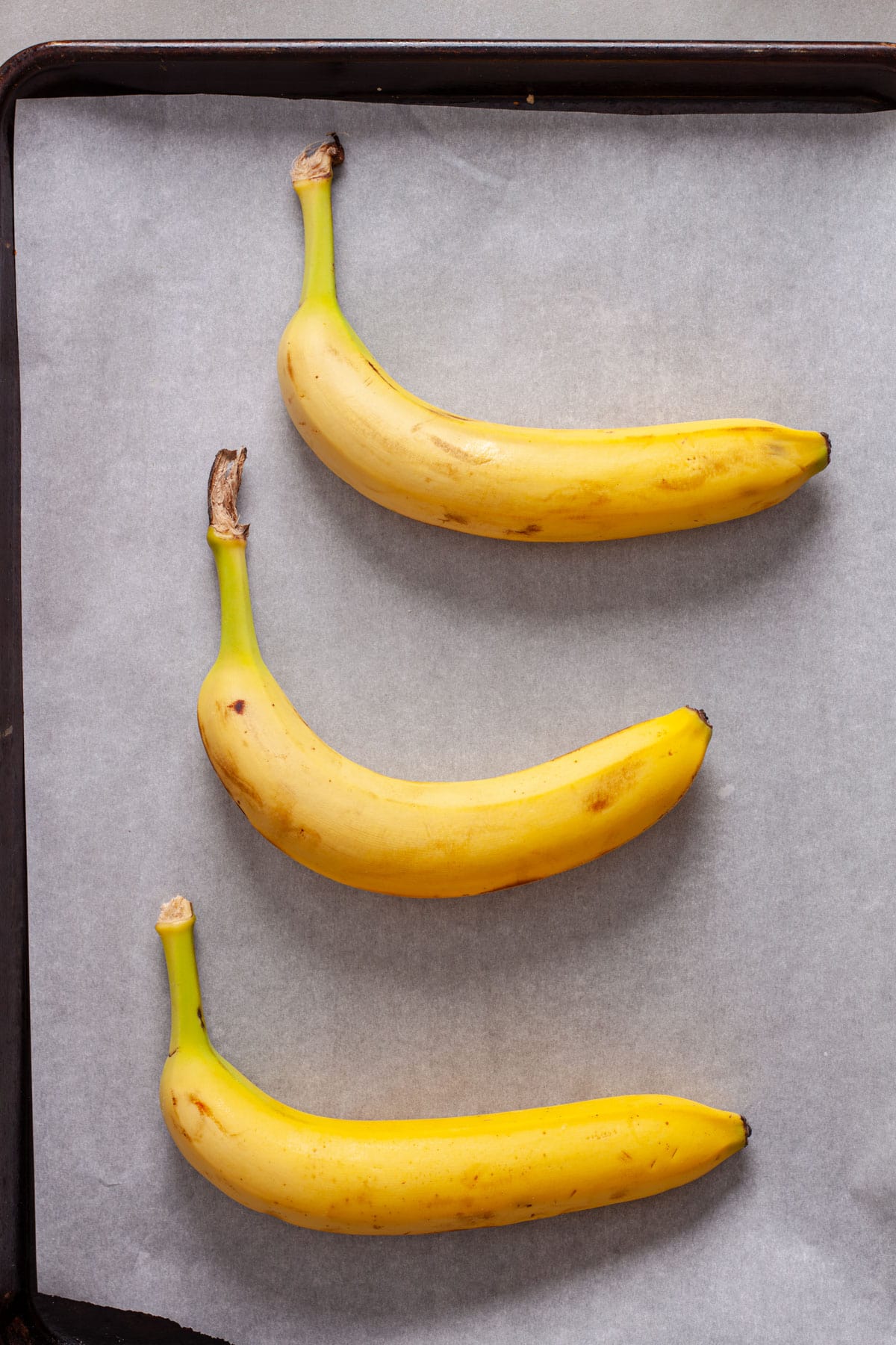 Bananas on a parchment lined baking sheet.