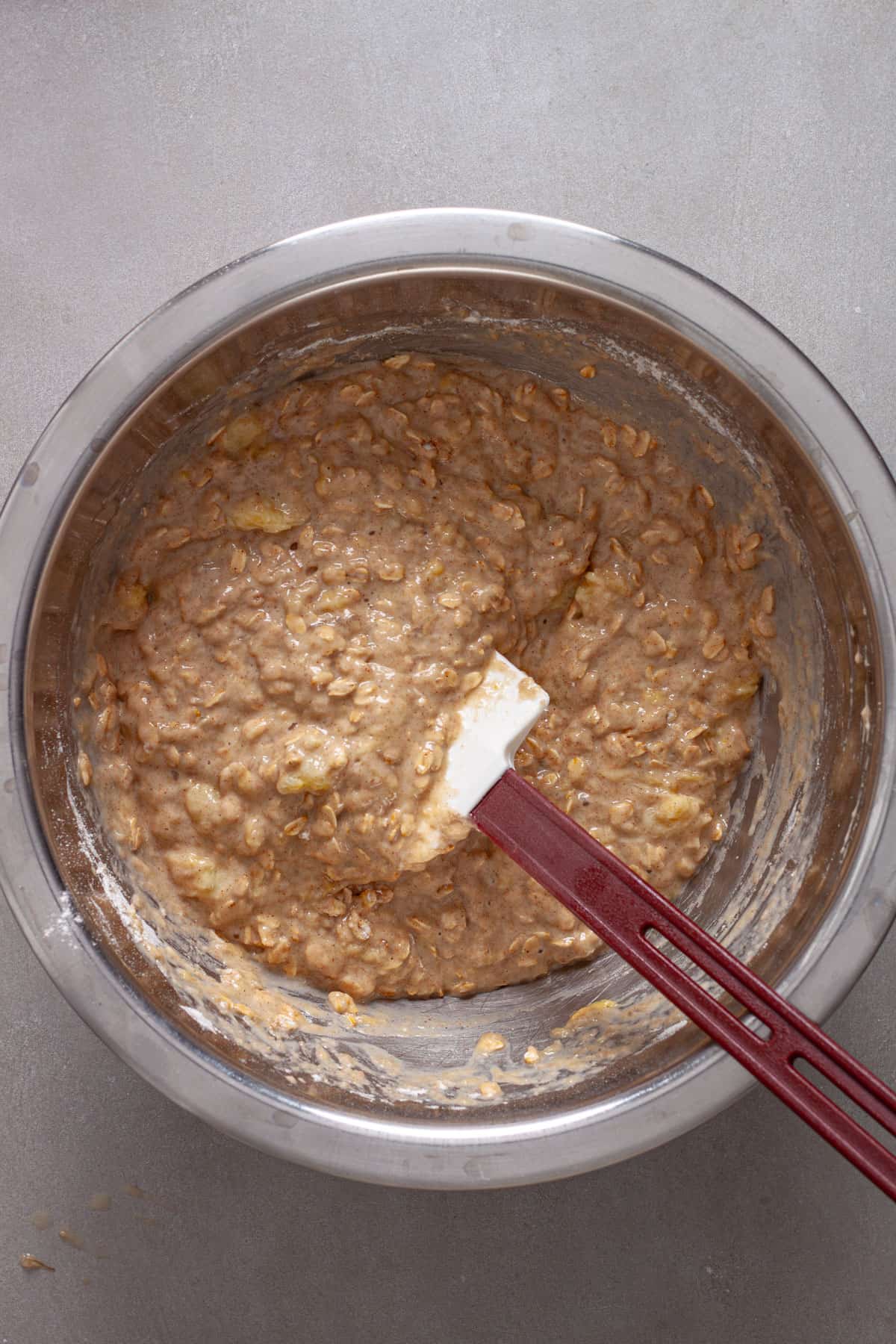 Batter for banana oatmeal muffins in a mixing bowl getting stirred by a spatula.