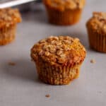 Banana oat muffins on a gray table with a muffin tin of more muffins in the background.
