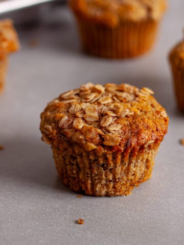 Banana oat muffins on a gray table with a muffin tin of more muffins in the background.