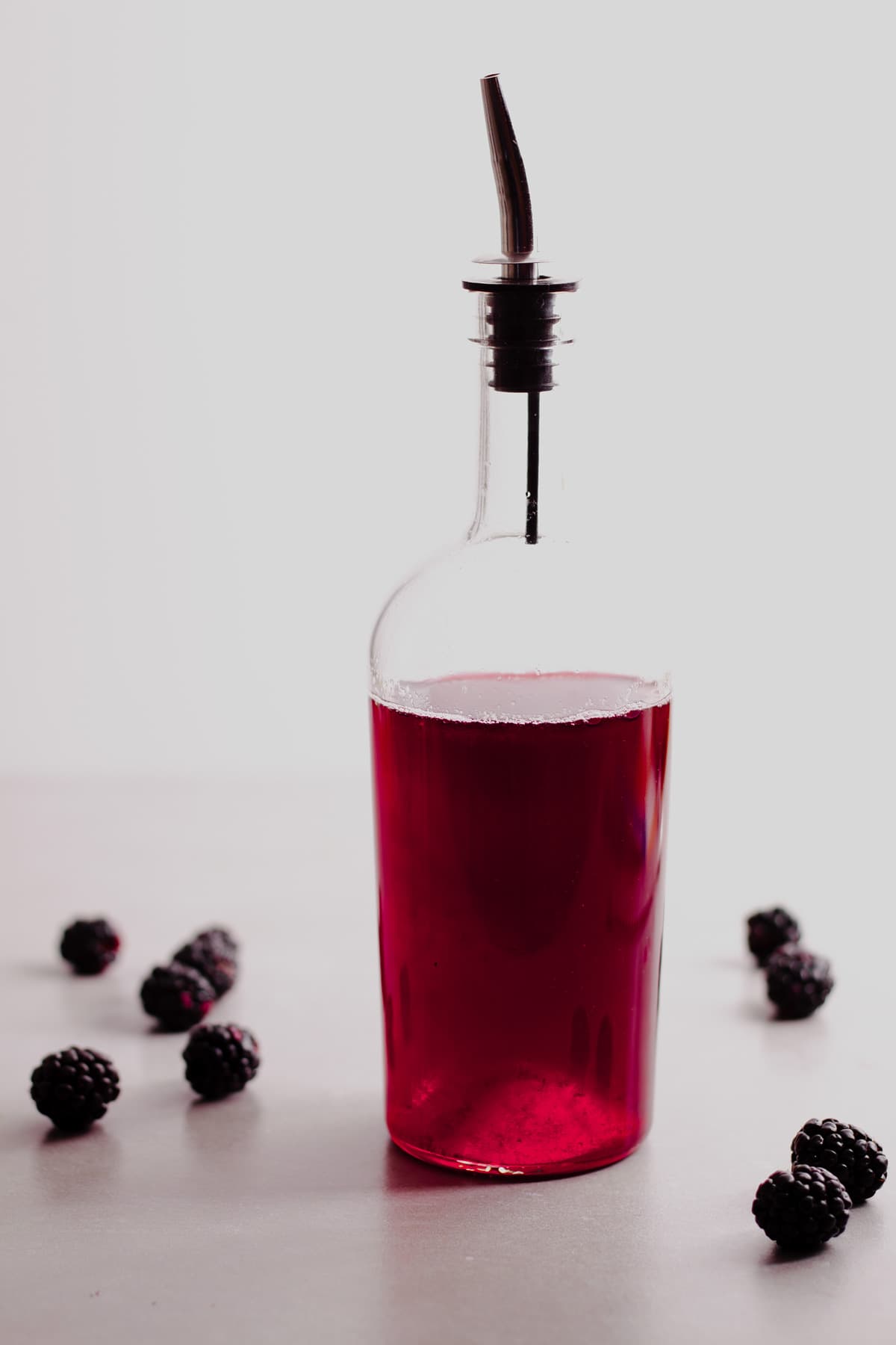 A glass bottle with a dark red blackberry simple syrup and fresh blackberries to the side.