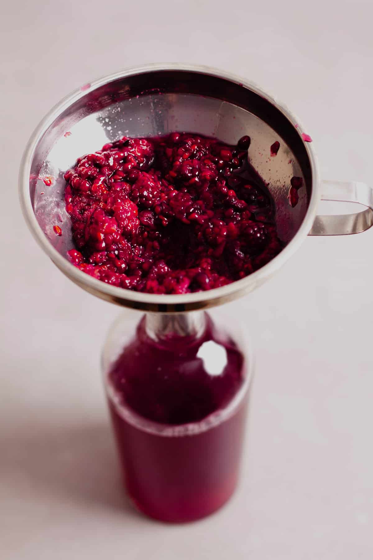 Cooked blackberries in a strainer over a glass jar for blackberry simple syrup.