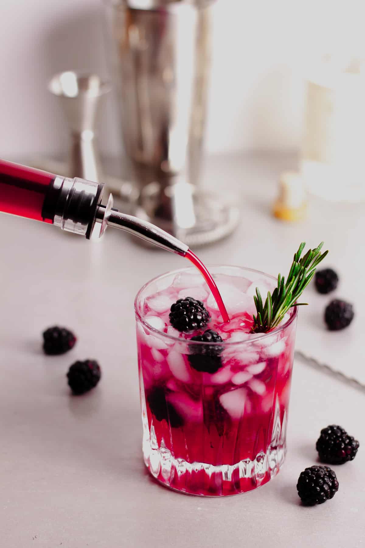Blackberry simple syrup pouring into a glass of ice with a sprig of rosemary and ice.