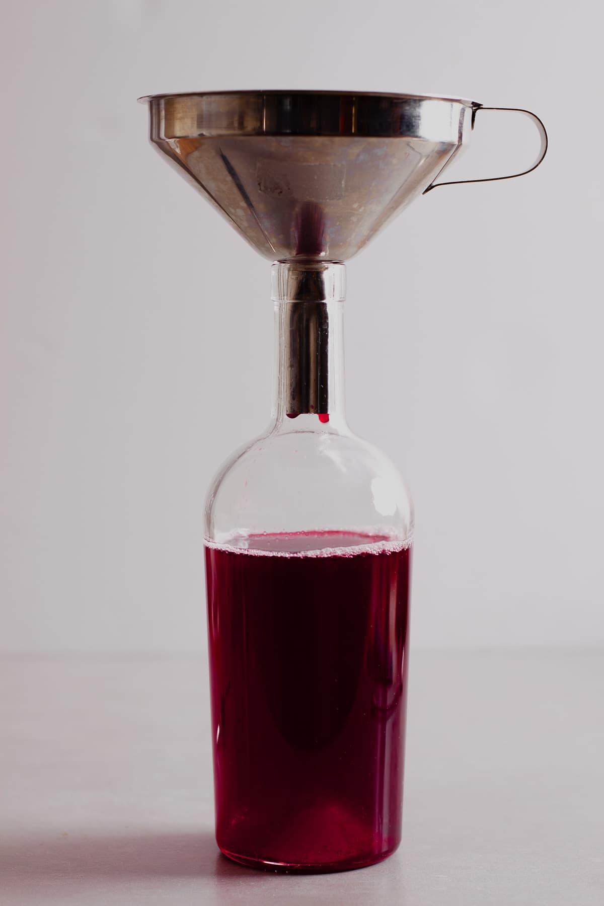 A funnel over a glass syrup jar filled with blackberry simple syrup.