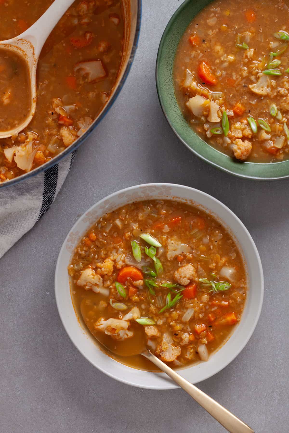 Two servings of lentil soup with cauliflower in bowls on a gray table.
