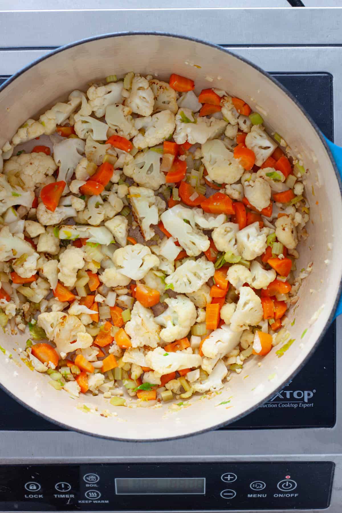 Cauliflower and other vegetables cooking in a large Dutch oven pot.