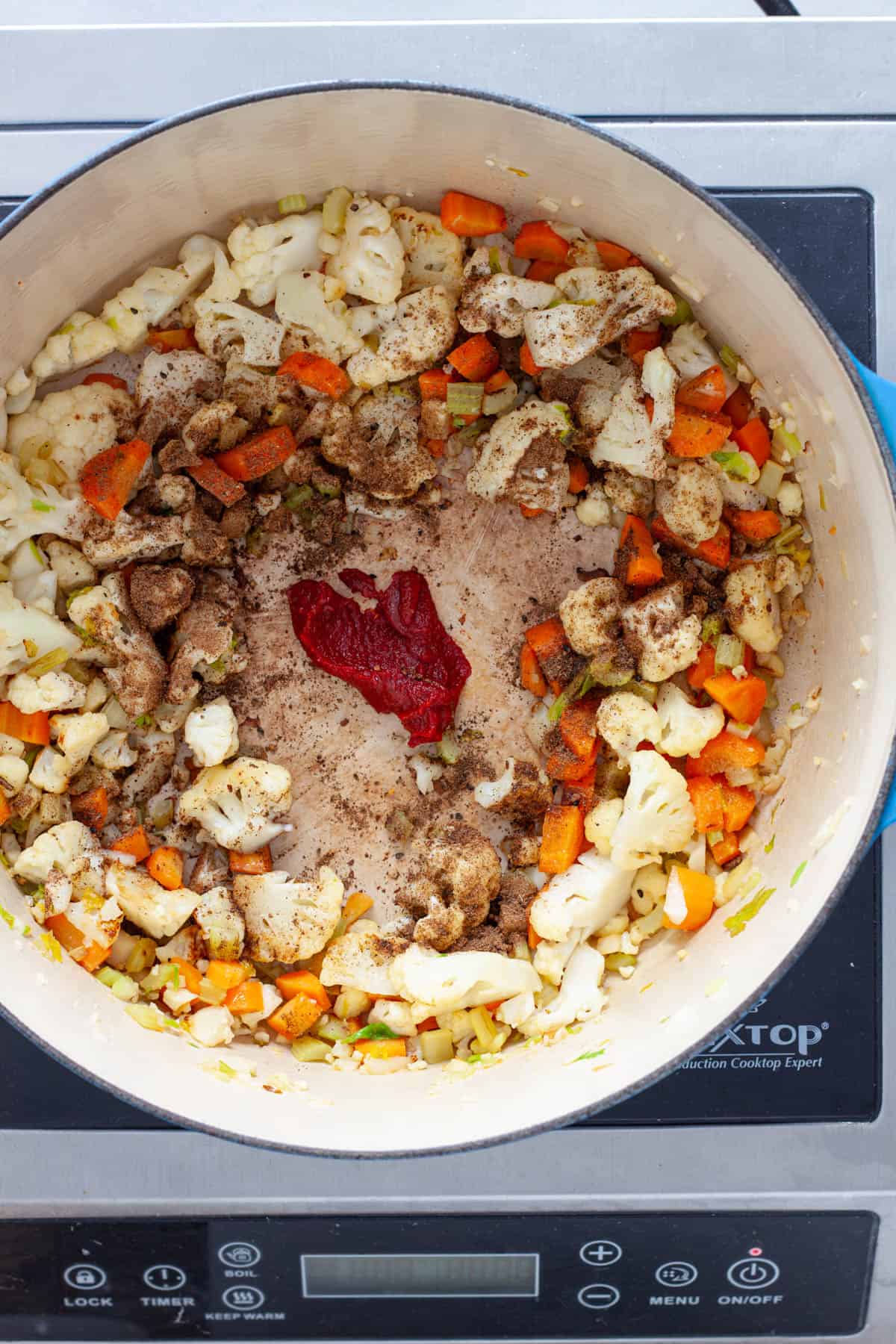 Tomato paste and spices added to a large Dutch oven with vegetables.
