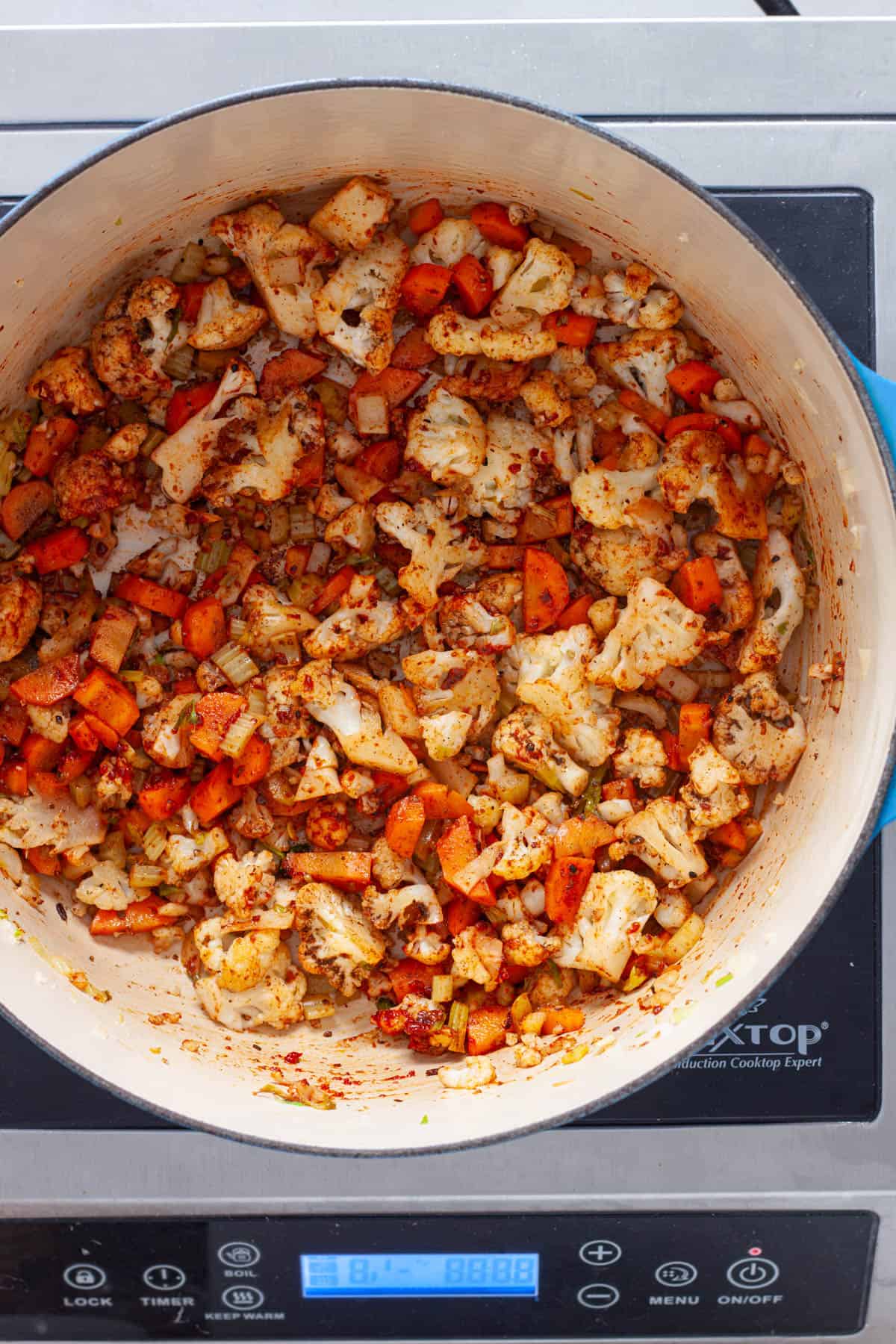 Cauliflower and other vegetables coated in spices and tomato paste cooking in a Dutch oven.