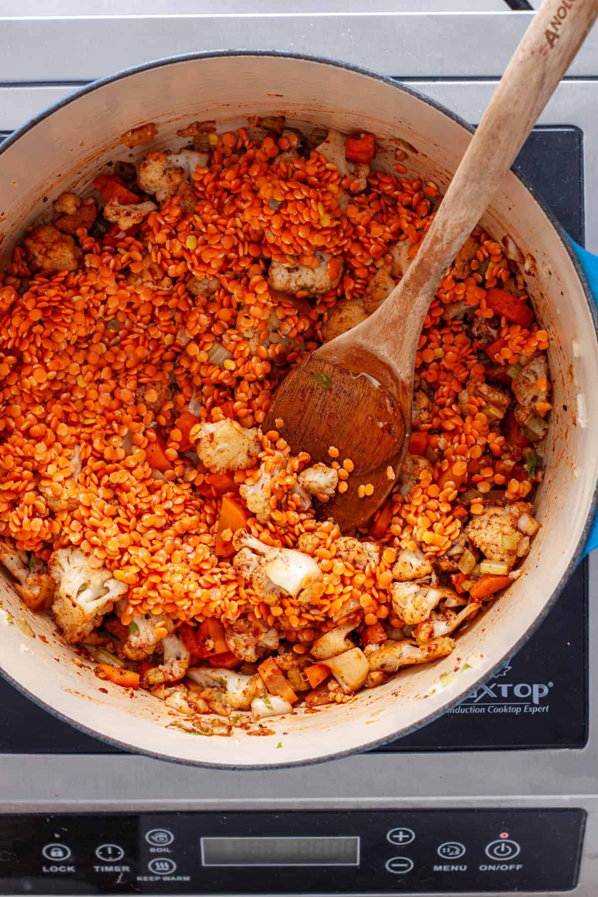 Red lentils added to a Dutch oven with vegetables for a homemade soup.