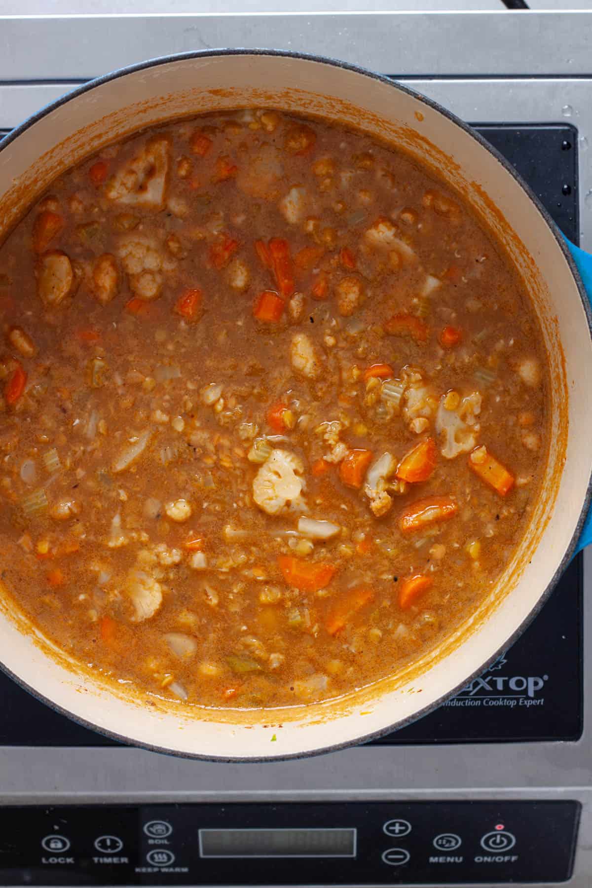 A homemade lentil soup with cauliflower and other vegetables in a Dutch oven.