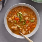 A bowl of cauliflower and lentil soup topped with scallions on a gray table.