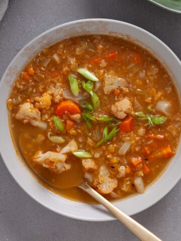 A bowl of cauliflower and lentil soup topped with scallions on a gray table.