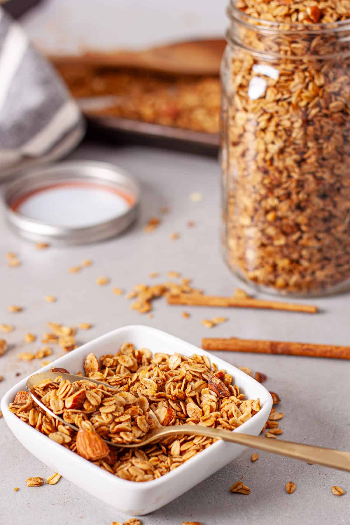 A small bowl of cinnamon granola with a bigger jar of granola in the background.
