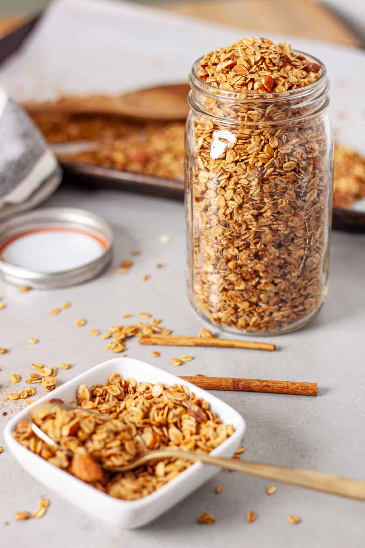 Homemade cinnamon granola in a large mason jar with a small bowl in the foreground.