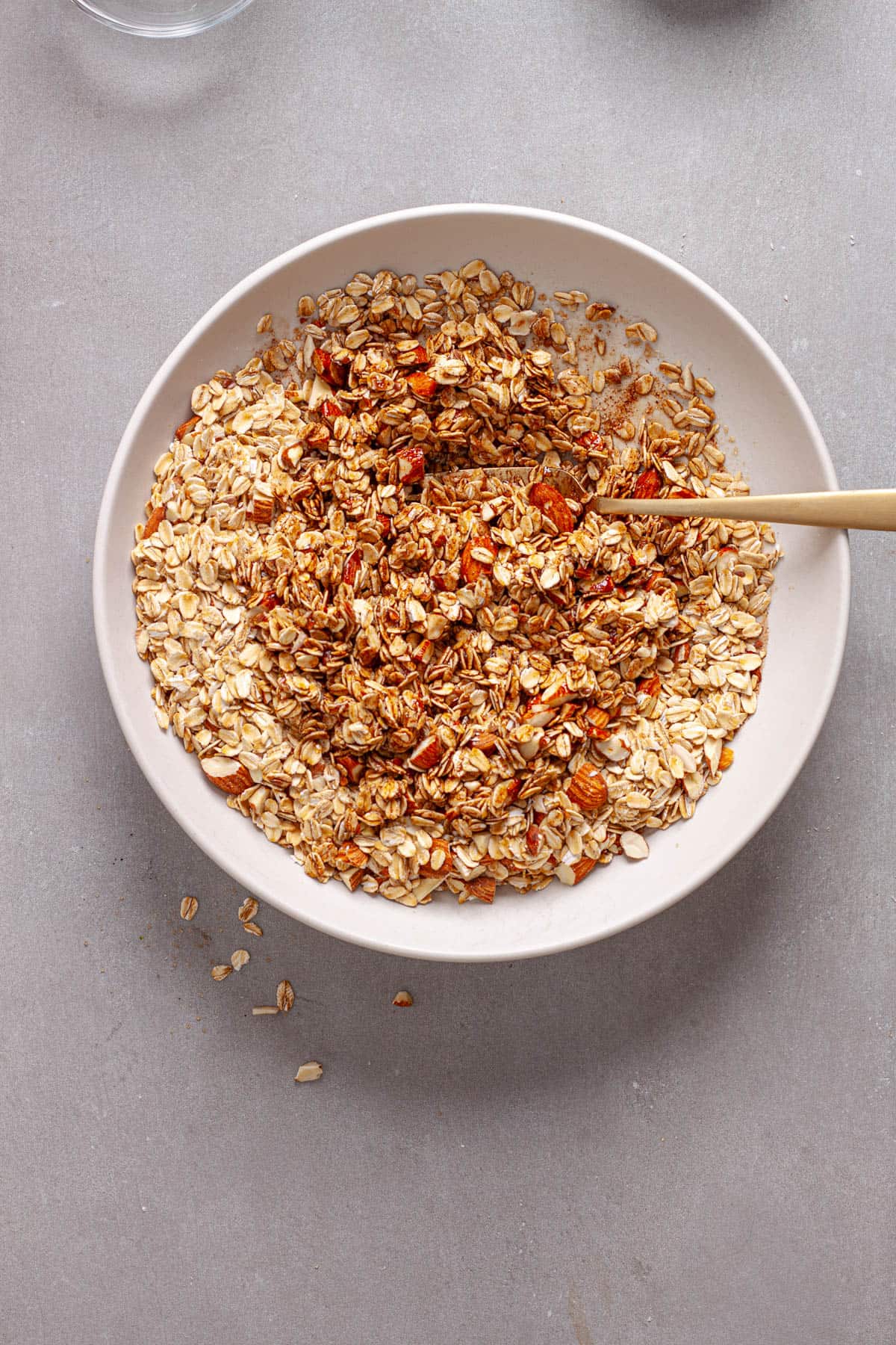 Rolled oats and nuts getting stirred with maple syrup and oil for homemade granola.