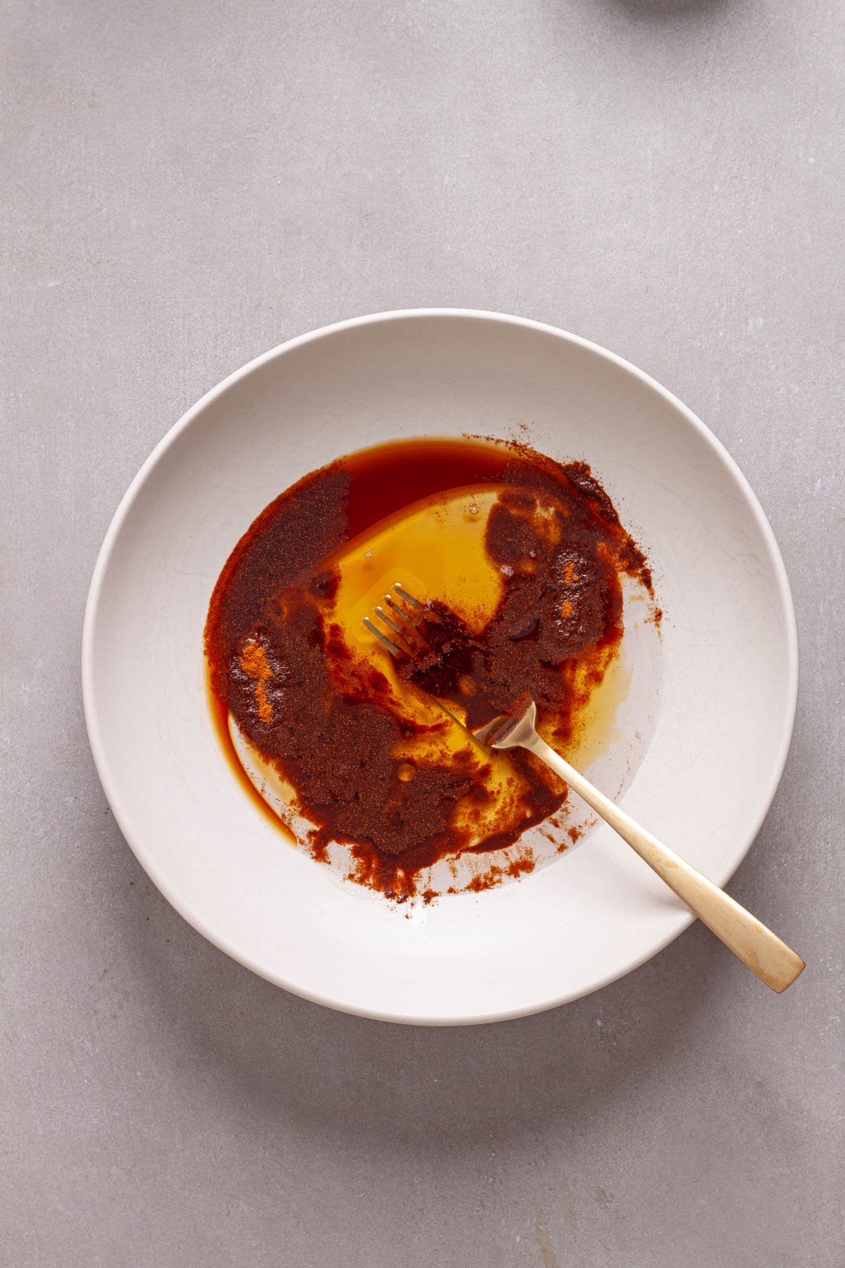 The wet ingredients for cinnamon granola in a bowl getting stirred by a fork.