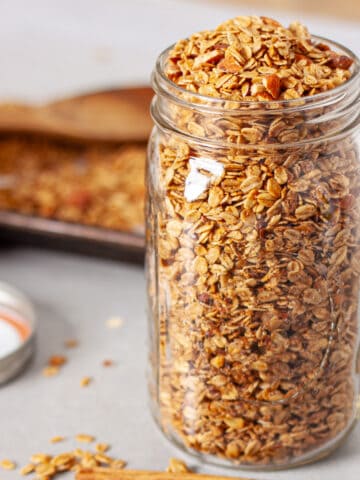 A large mason jar of homemade cinnamon granola on a gray table.