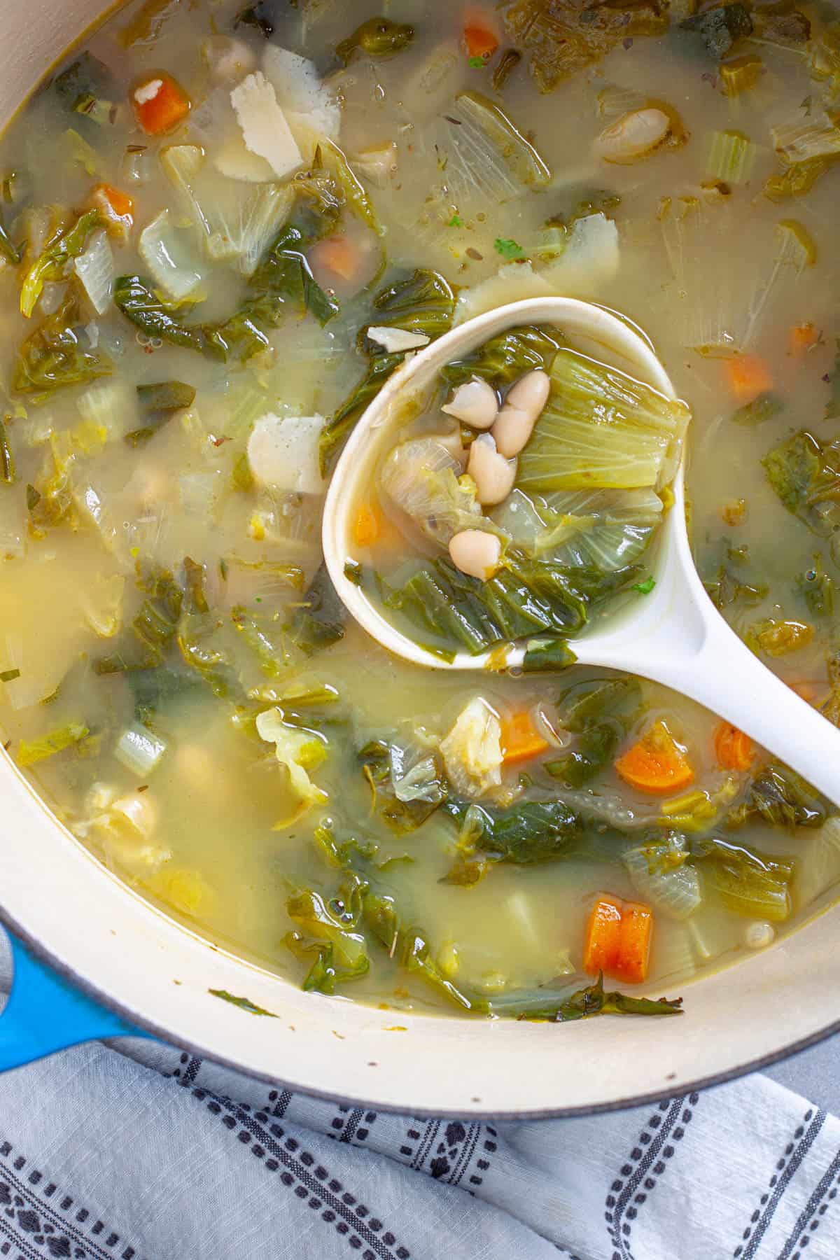 A ladle in a Dutch oven with escarole and white bean soup.