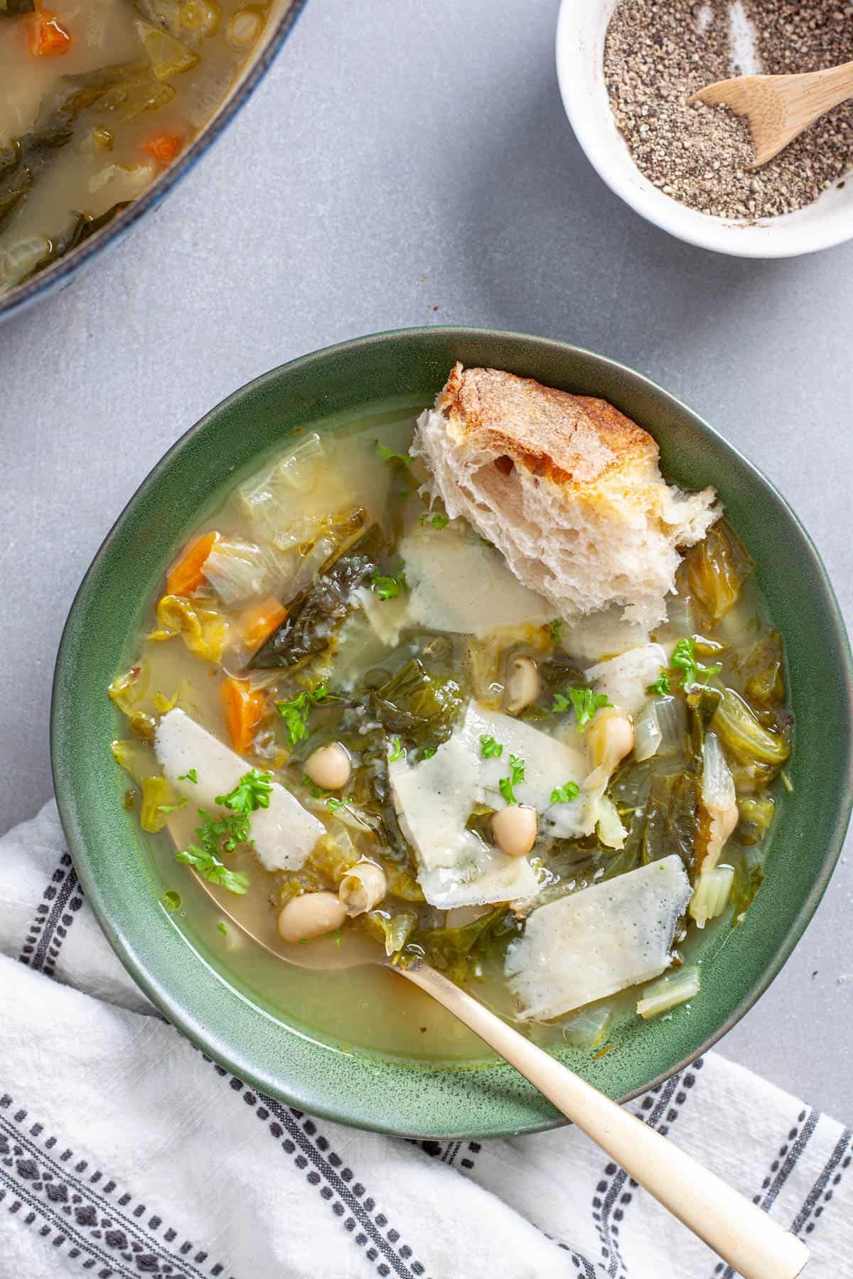 A bowl of escarole and white bean soup with parmesan cheese and crusty bread for garnish.