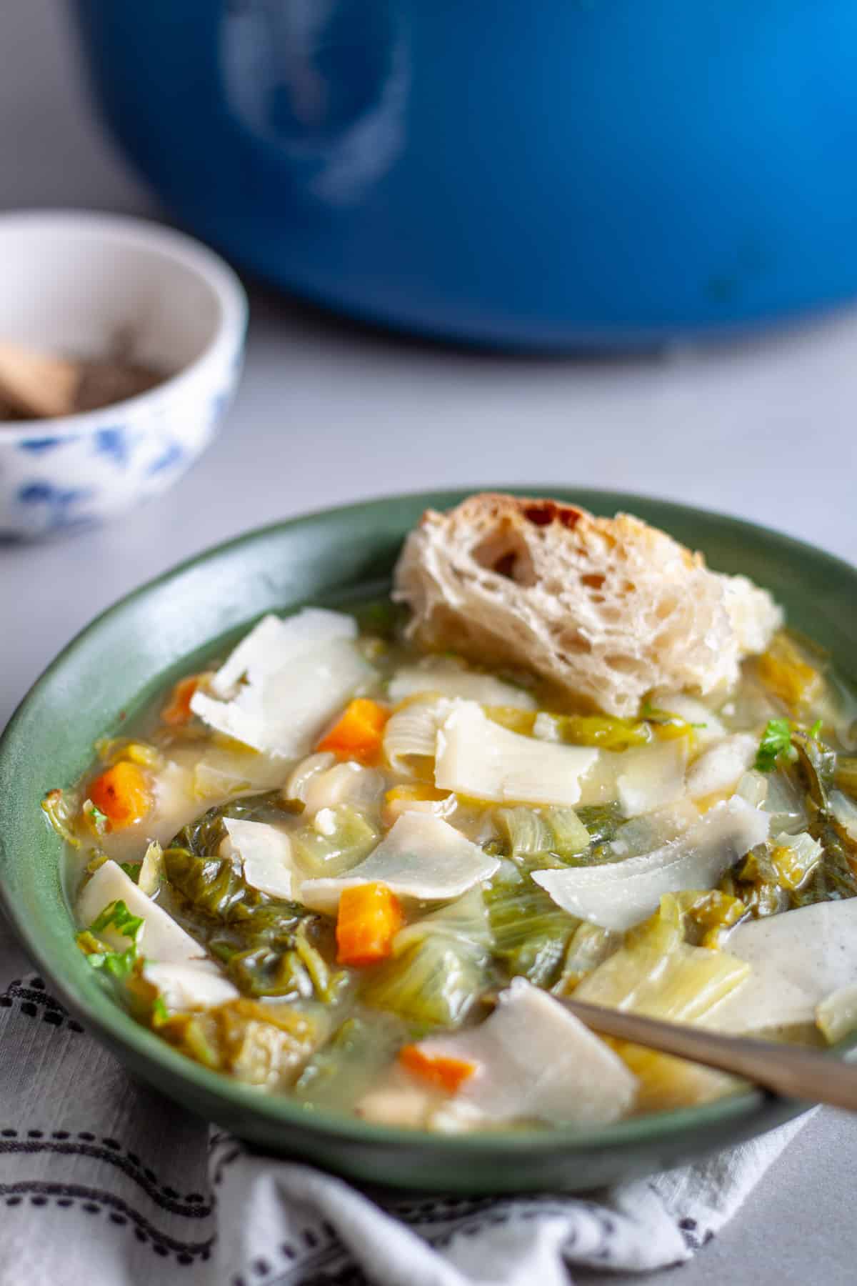 A green bowl of escarole and white bean soup sopped with parmesan cheese and crusty bread as a garnish.