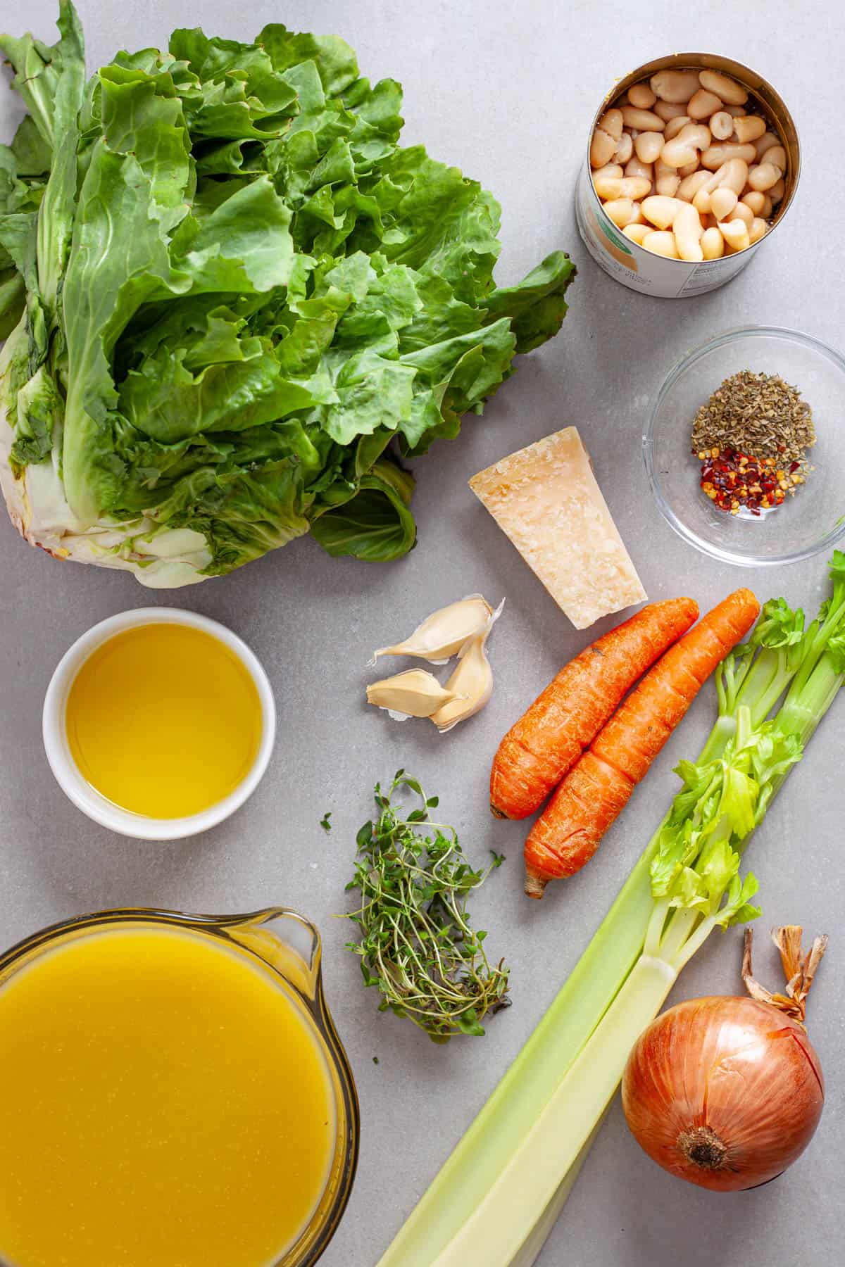 Ingredients for escarole and white bean soup on a gray table.