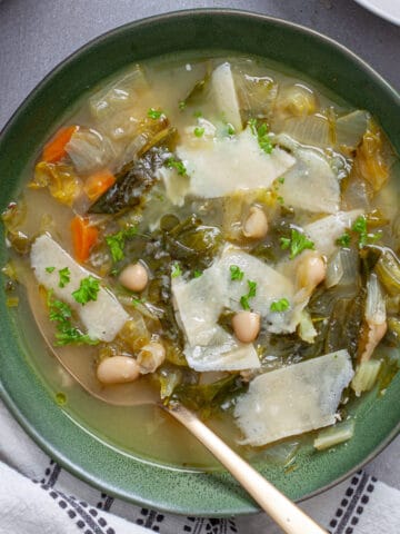 A bowl of escarole and white bean soup with parmesan cheese for garnish.