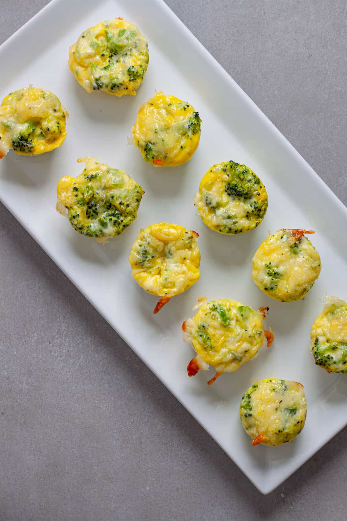 A tray of mini broccoli and cheddar egg bites on a gray table.