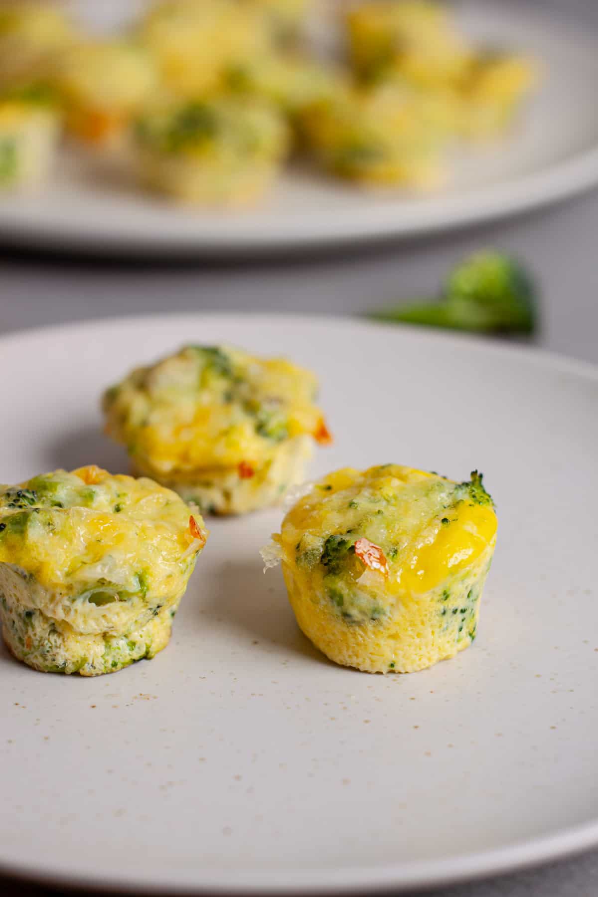 A small plate of mini broccoli and cheddar egg bites with more in the background.