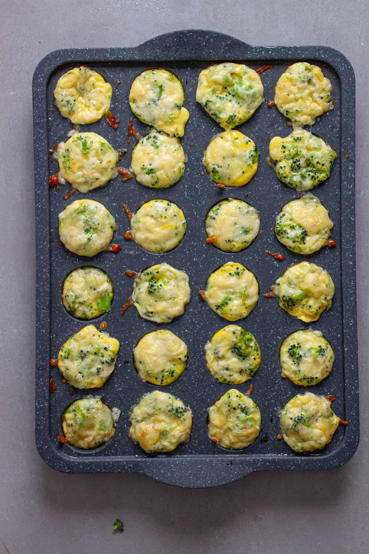 Puffy cooked mini broccoli and cheddar egg bites in a mini muffin pan.