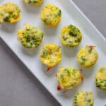A tray of mini broccoli and cheddar egg bites on a gray table.