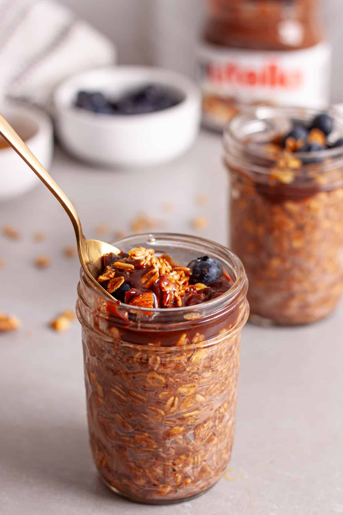 A spoon in a small mason jar of Nutella overnight oats on a gray table.