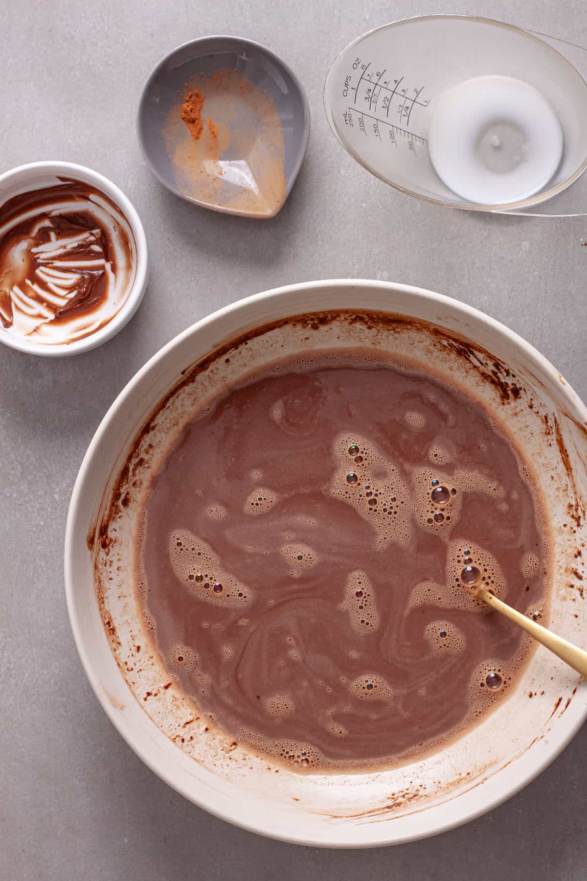 Milk, cocoa powder and nutella getting stirred together in a white mixing bowl.