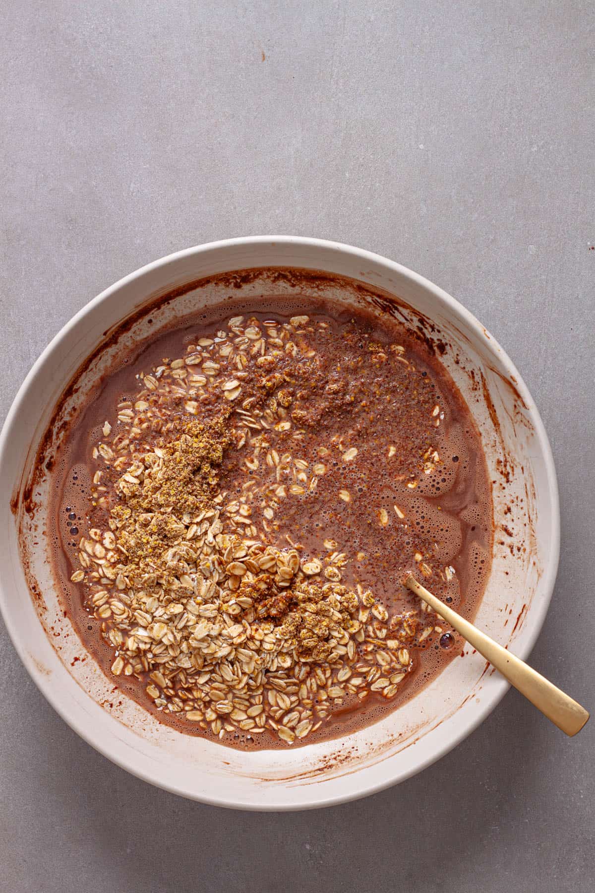 Milk and nutella in a mixing bowl with rolled oats and flaxseeds getting stirred in.