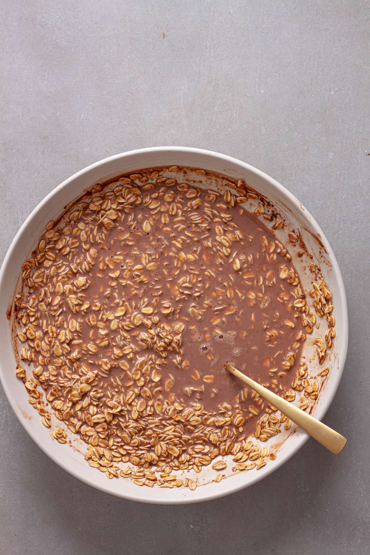 Rolled oats soaking in a chocolate milk mixture in a white bowl.
