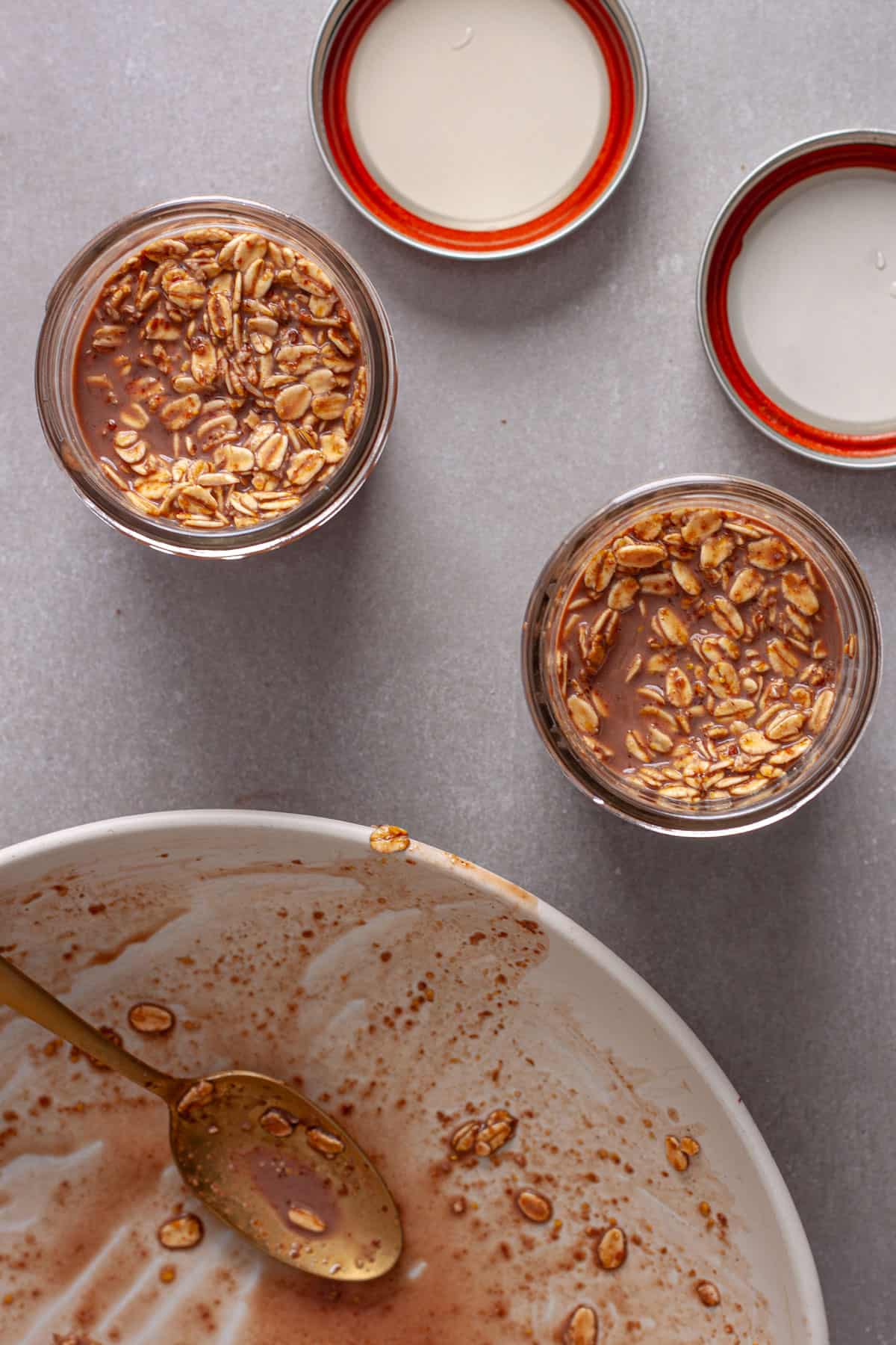 Oats and chocolate milk getting added to small mason jars for Nutella overnight oats.