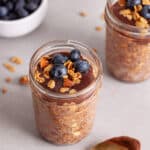 A single mason jar portion of Nutella overnight oats topped with blueberries and granola.
