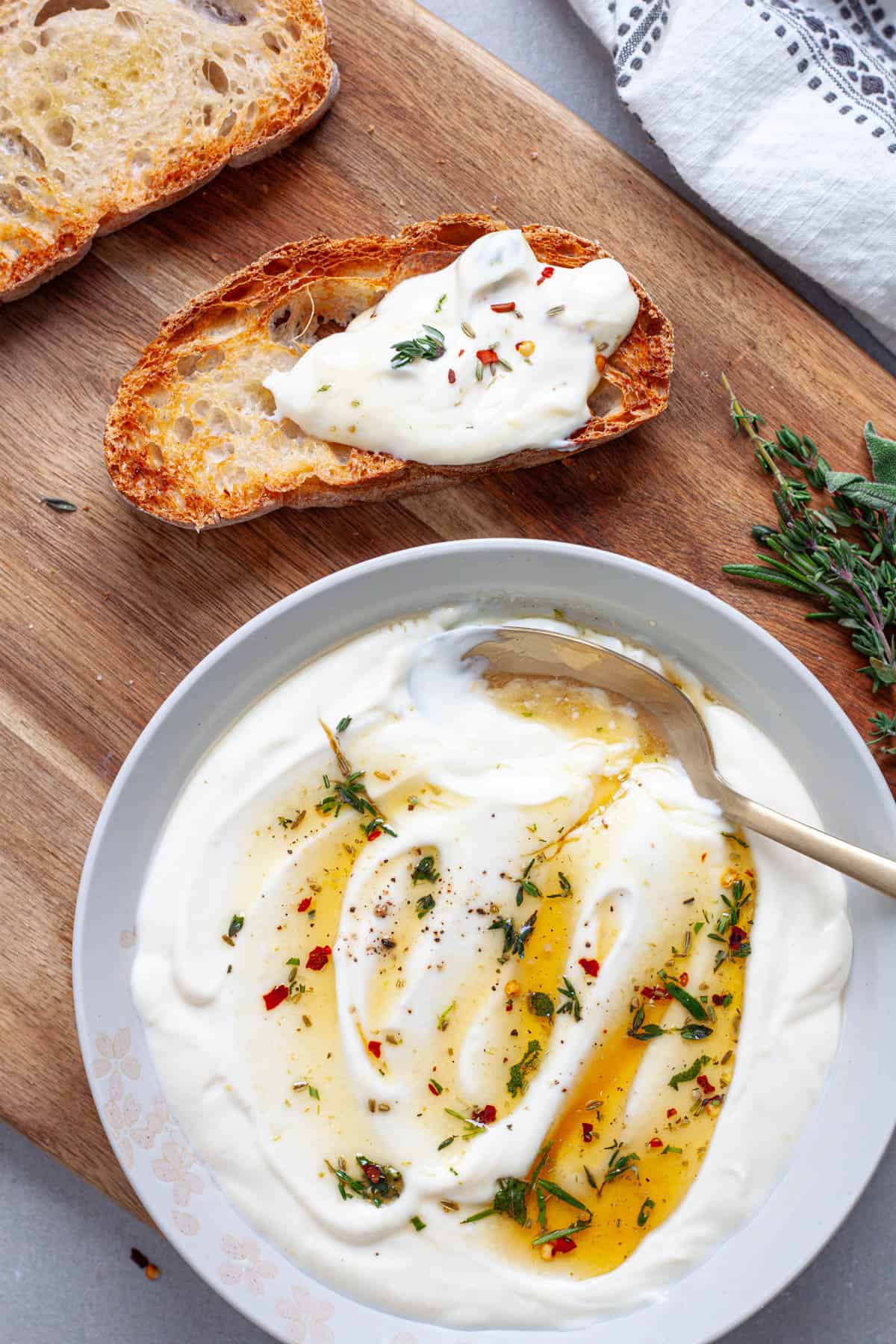 A cutting board with a piece of toast topped with whipped ricotta with a ricotta dip to the side.