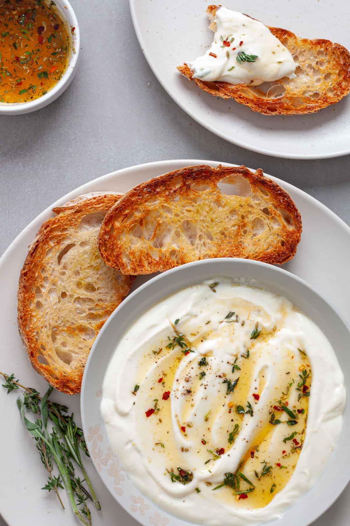 A platted of toasted bread with whipped ricotta dip topped with honey and herbs and a serving to the side.
