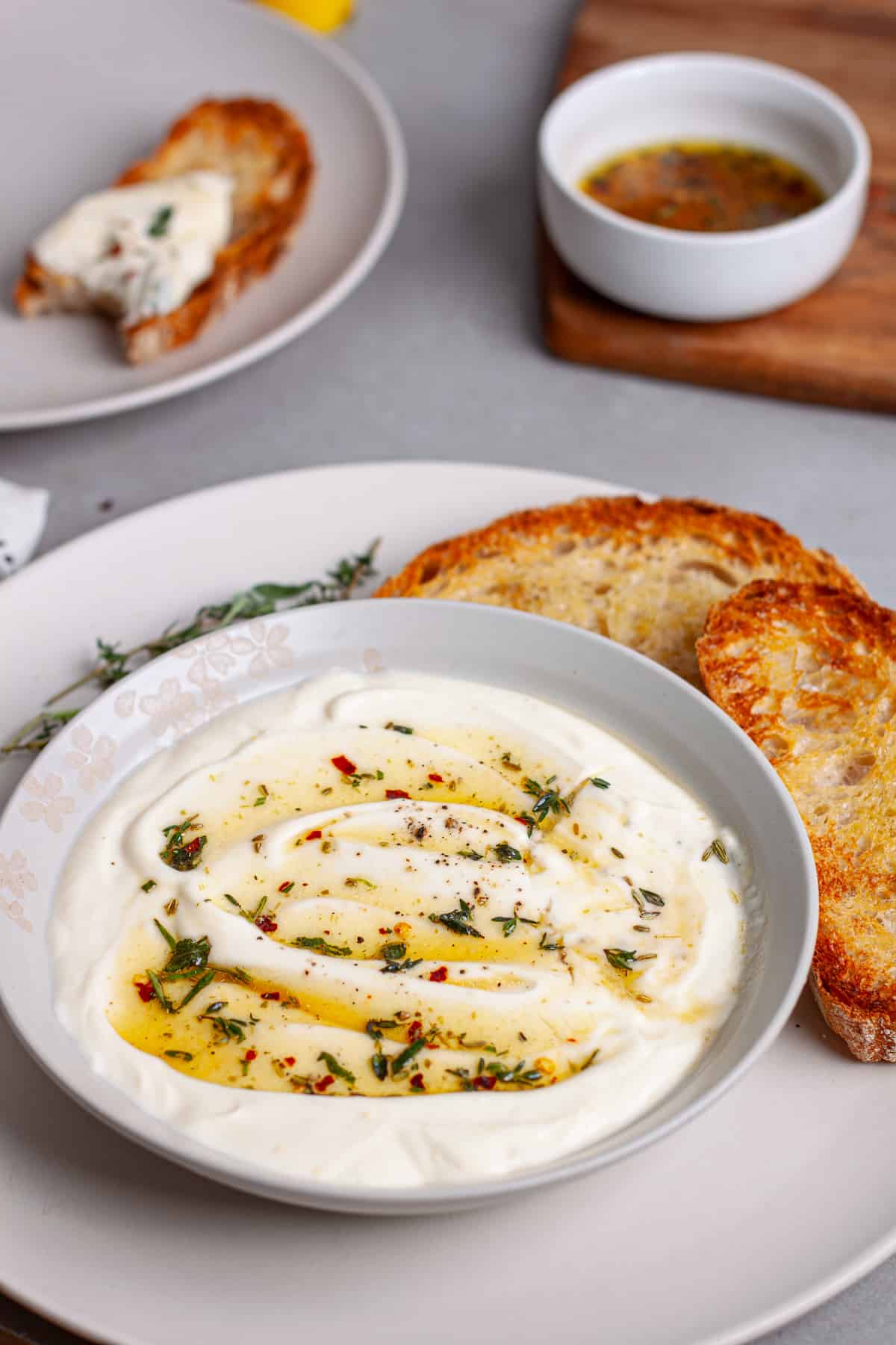 A serving bowl of whipped ricotta dip topped with honey and herbs on a plate with toasted bread.