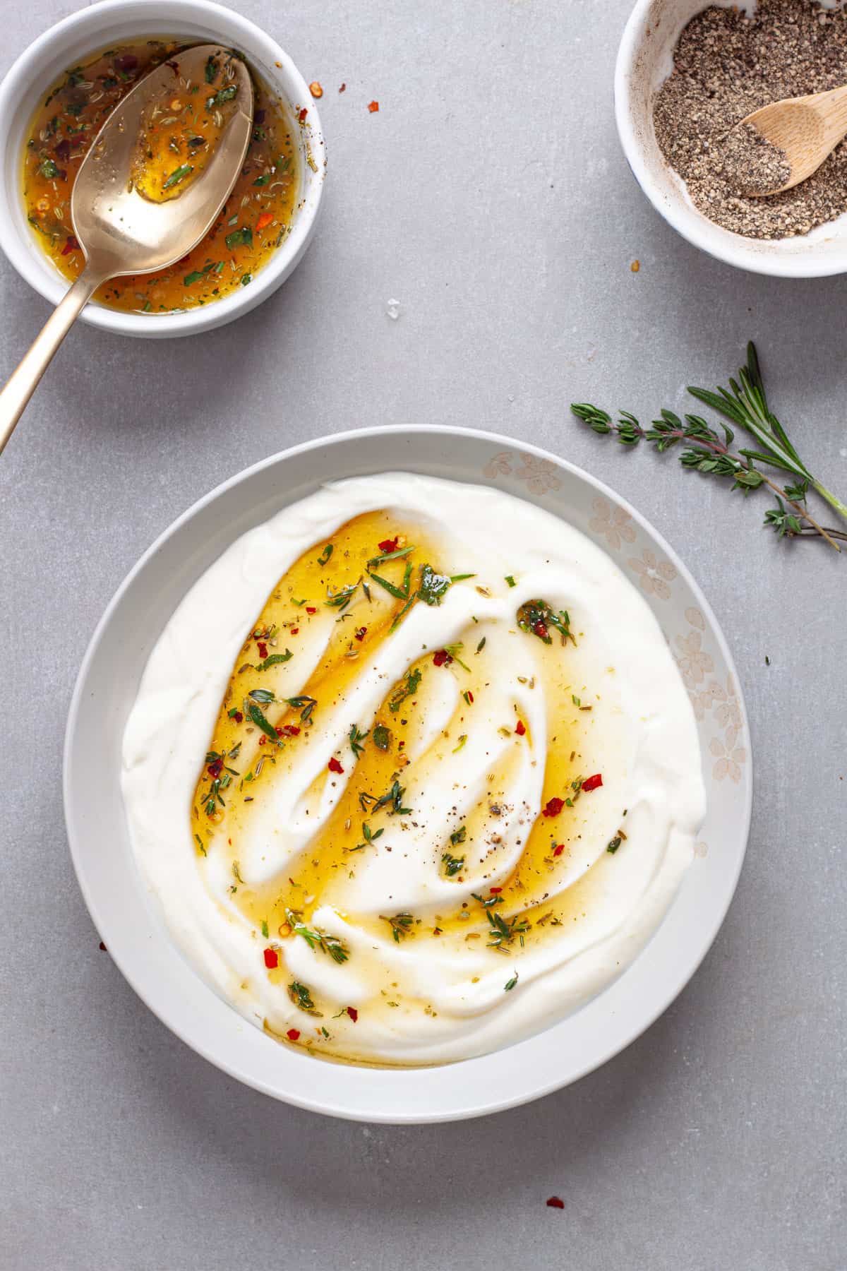A serving bowl of whipped ricotta cheese dip topped with honey and herbs on a gray table.