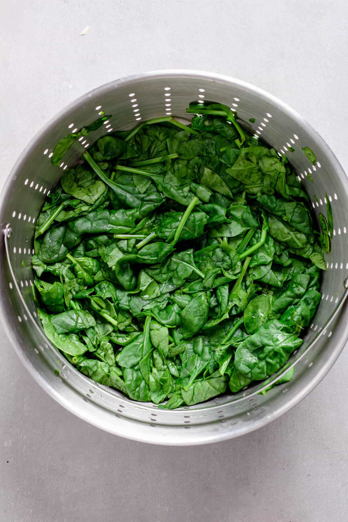 Wilted spinach in a strainer on a gray table.