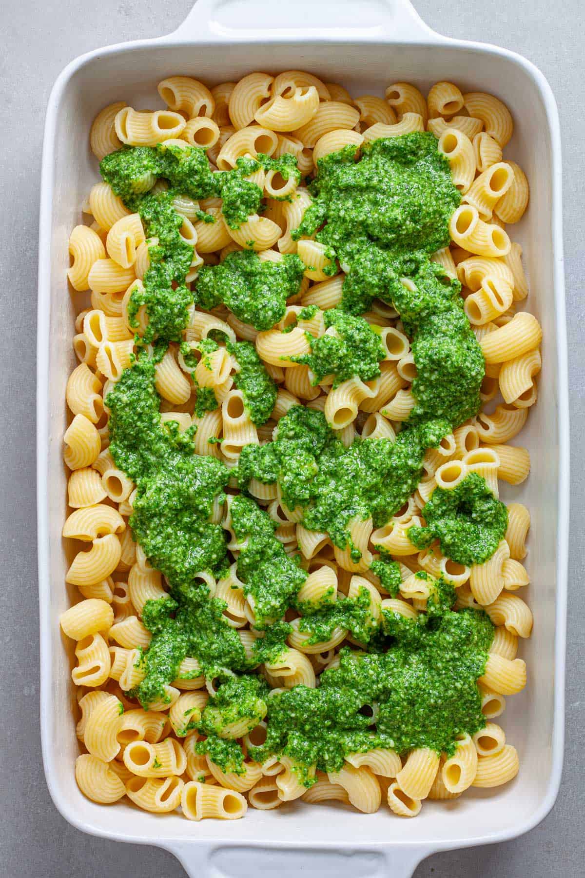 A casserole dish of cooked pasta with pesto spooned on top.